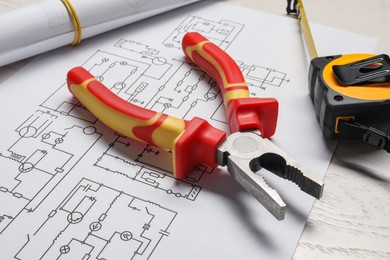 Wiring diagram, pliers and tape measure on white wooden table, closeup