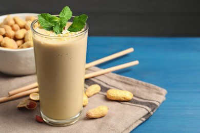 Photo of Glass of tasty banana smoothie with peanuts and mint on light blue wooden table, closeup. Space for text