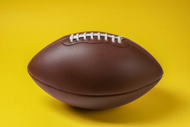 Photo of Brown leather American football ball on yellow background, closeup