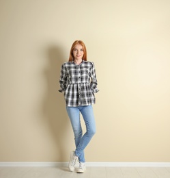 Young woman in stylish jeans near light wall