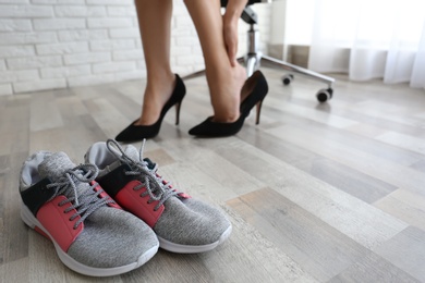 Woman changing shoes in office, closeup with focus on sneakers. Tired feet after wearing high heels