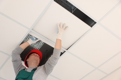 Photo of Suspended ceiling installation. Builder working with PVC tile, low angle view
