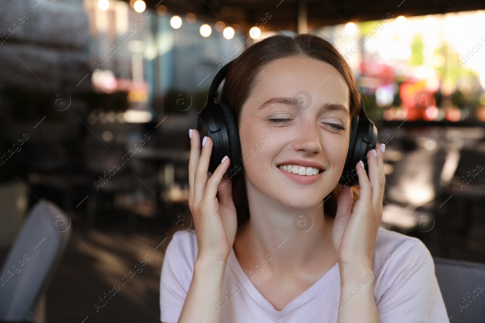 Photo of Smiling woman in headphones listening to music in outdoor cafe. Space for text