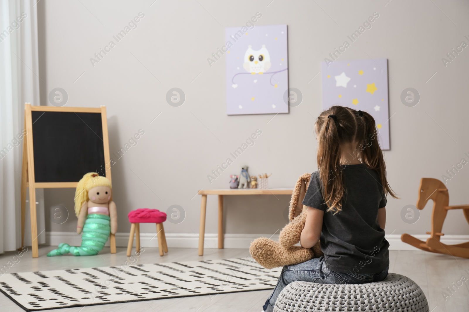 Photo of Lonely little girl with toy bunny at home, back view. Autism concept