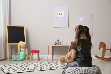 Photo of Lonely little girl with toy bunny at home, back view. Autism concept