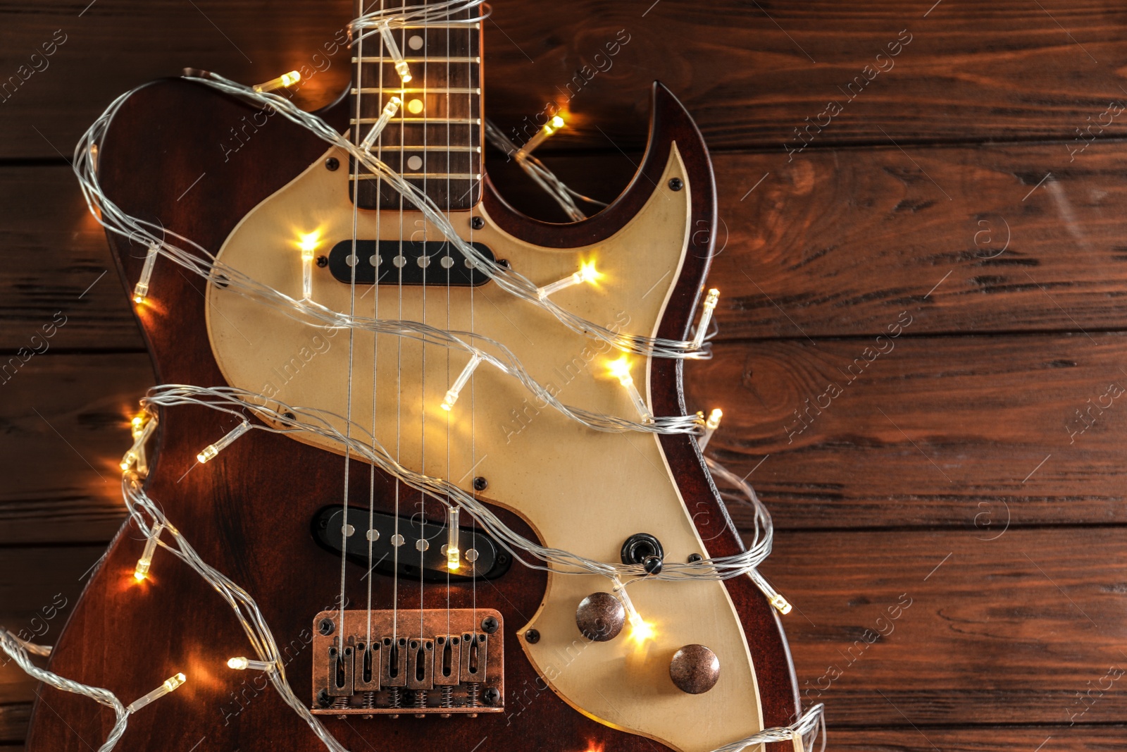 Photo of Guitar with fairy lights on wooden background, top view. Christmas music concept