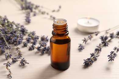 Photo of Bottle of essential oil and lavender flowers on white wooden table