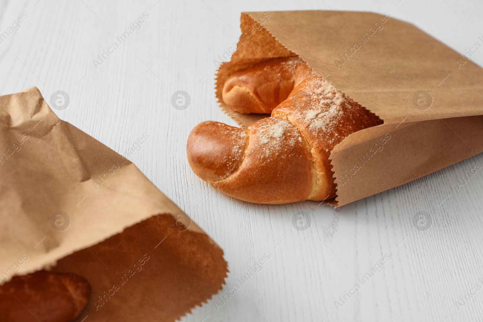 Photo of Paper bags with pastry on light wooden background. Space for text