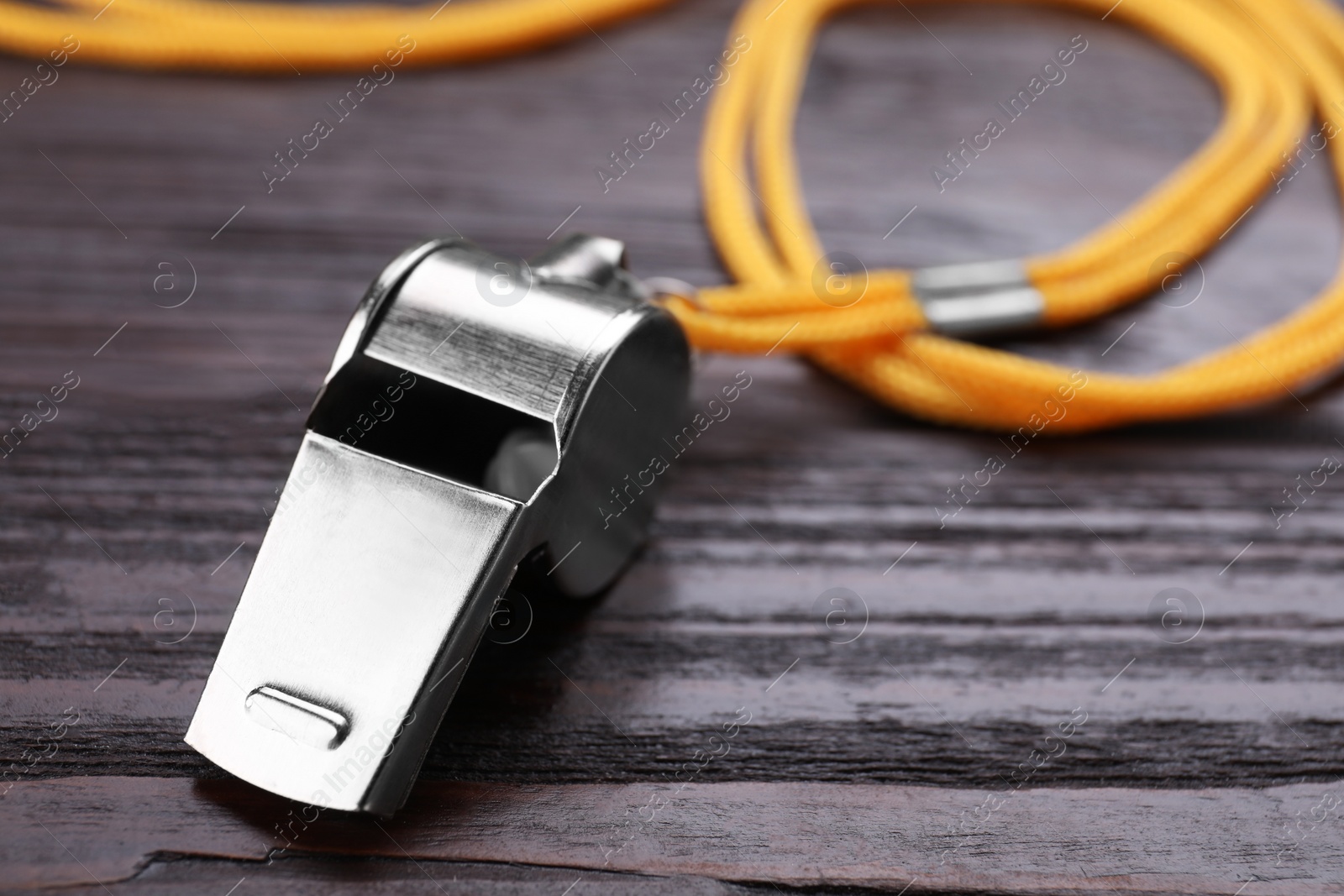 Photo of One metal whistle with cord on wooden table, closeup