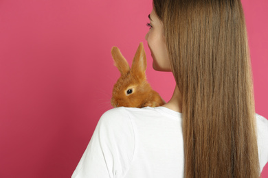 Photo of Young woman with adorable rabbit on pink background, closeup. Lovely pet