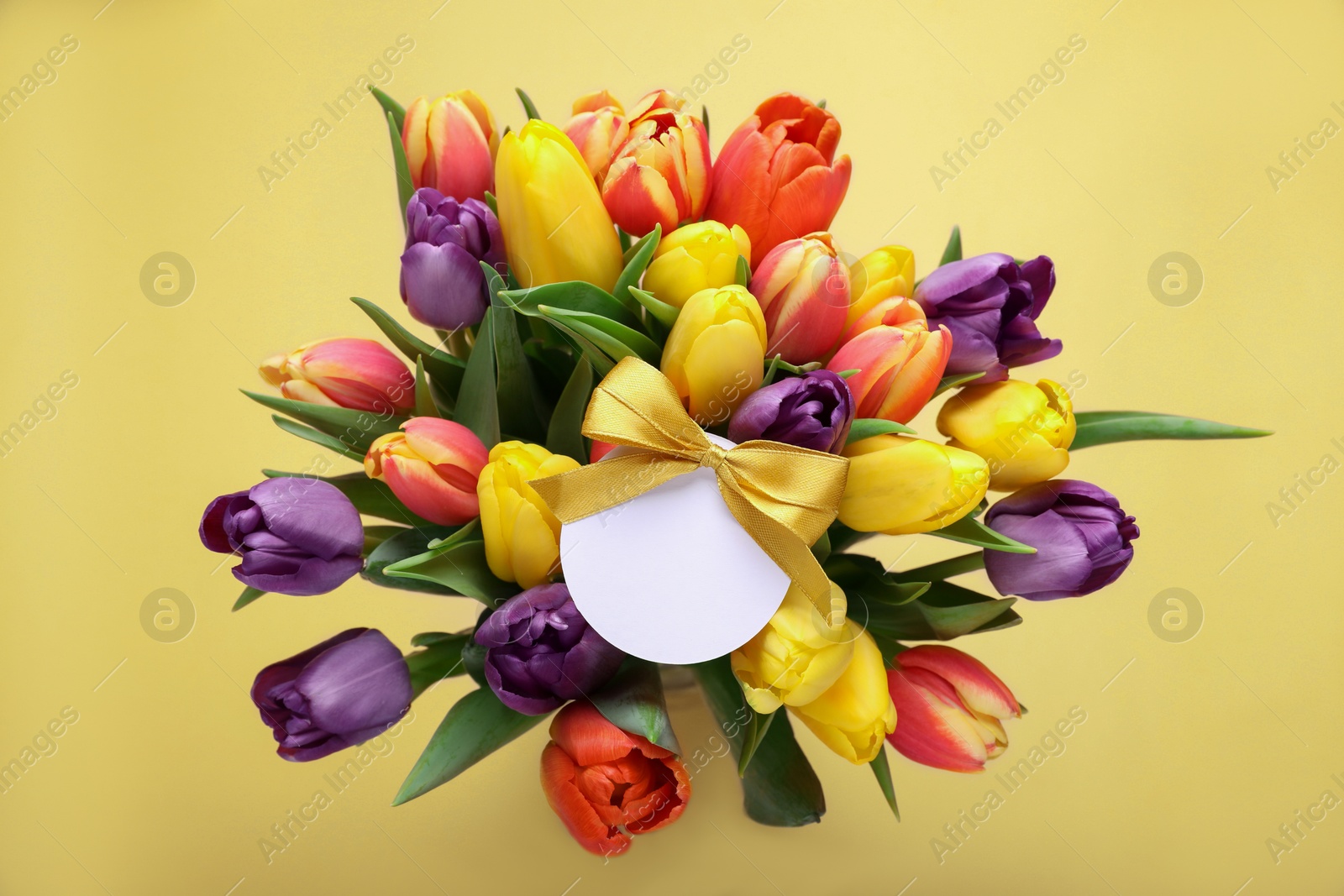 Photo of Bouquet of beautiful colorful tulips with blank card on beige background, top view. Birthday celebration