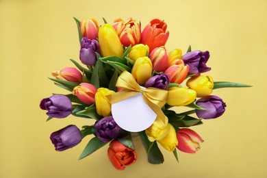 Bouquet of beautiful colorful tulips with blank card on beige background, top view. Birthday celebration