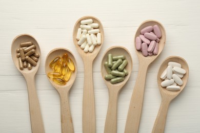 Photo of Different vitamin capsules in spoons on white wooden table, flat lay