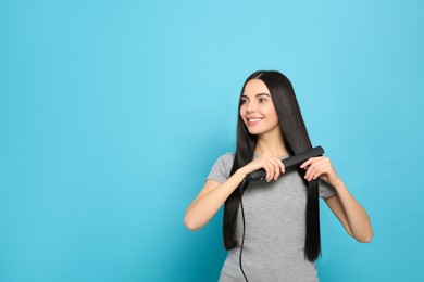 Beautiful happy woman using hair iron on light blue background. Space for text