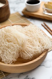 Photo of Bowl with uncooked rice noodles on white marble table, closeup