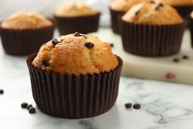 Delicious sweet muffin with chocolate chips on white marble table, closeup. Space for text