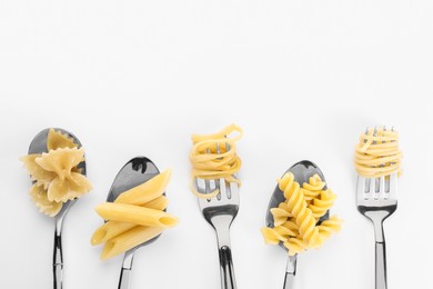 Forks and spoons with various tasty pasta on white background, flat lay. Space for text