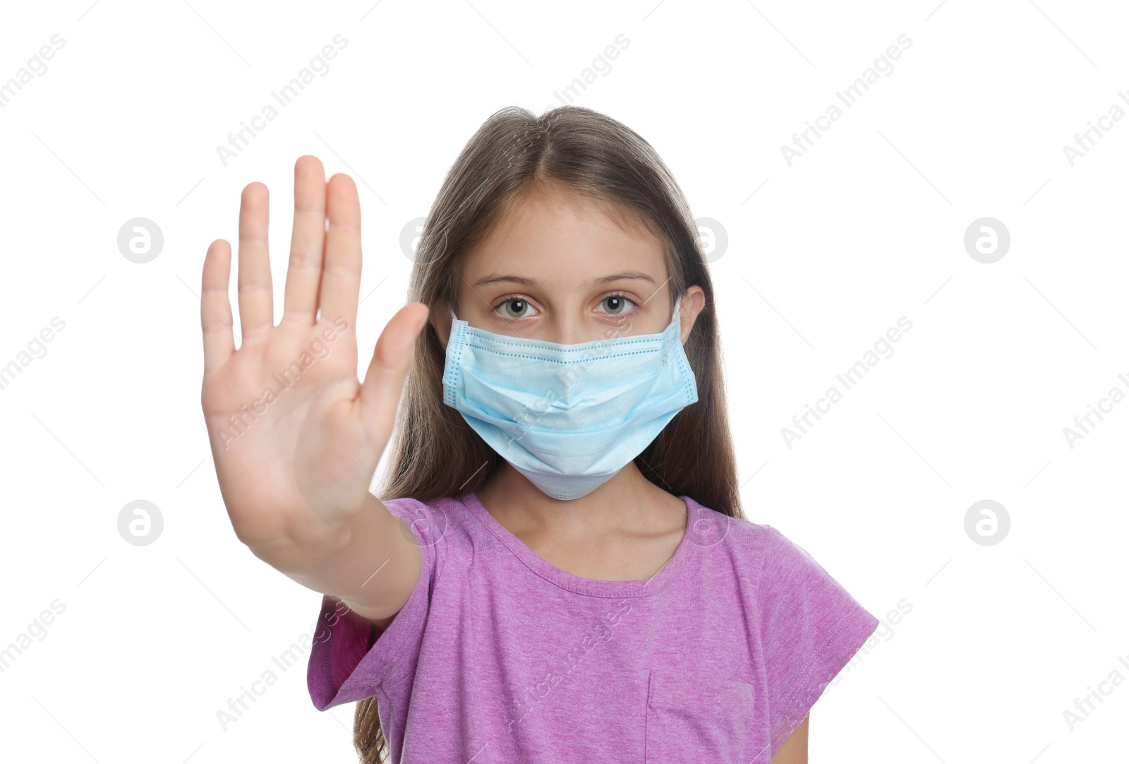 Photo of Little girl in protective mask showing stop gesture on white background. Prevent spreading of coronavirus