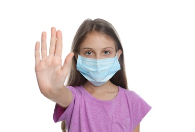 Photo of Little girl in protective mask showing stop gesture on white background. Prevent spreading of coronavirus