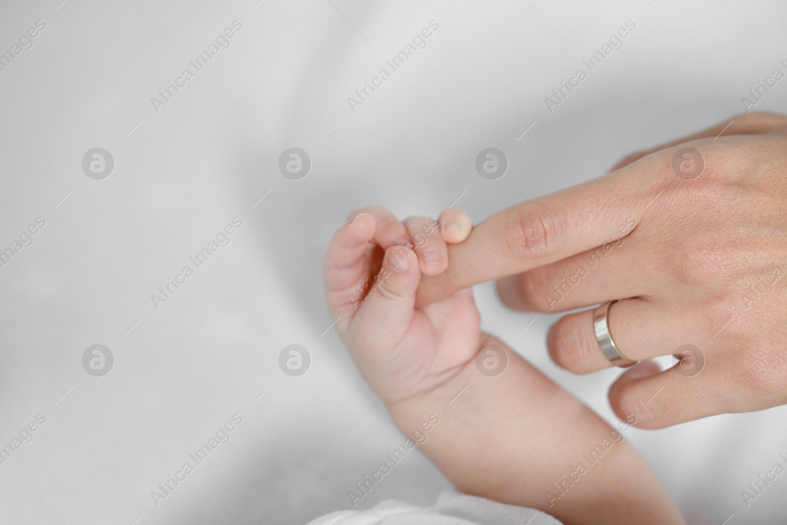 Photo of Baby holding motherʼs hand on bed, closeup