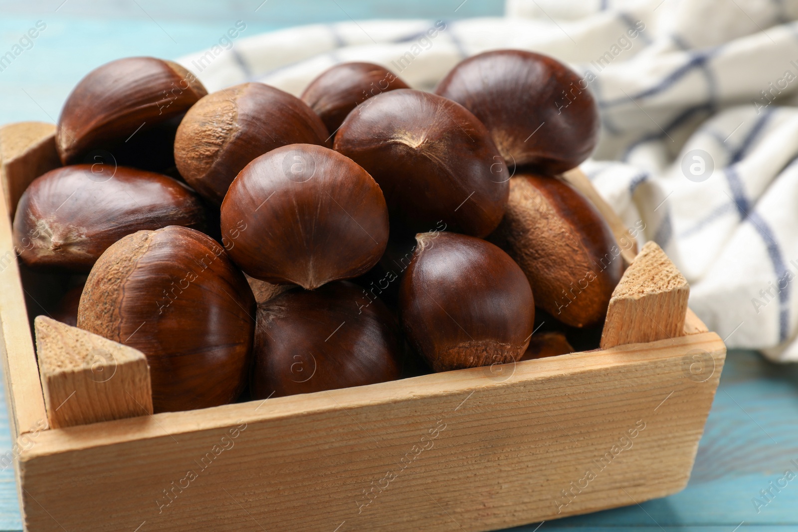 Photo of Roasted edible sweet chestnuts in crate on light blue table, closeup
