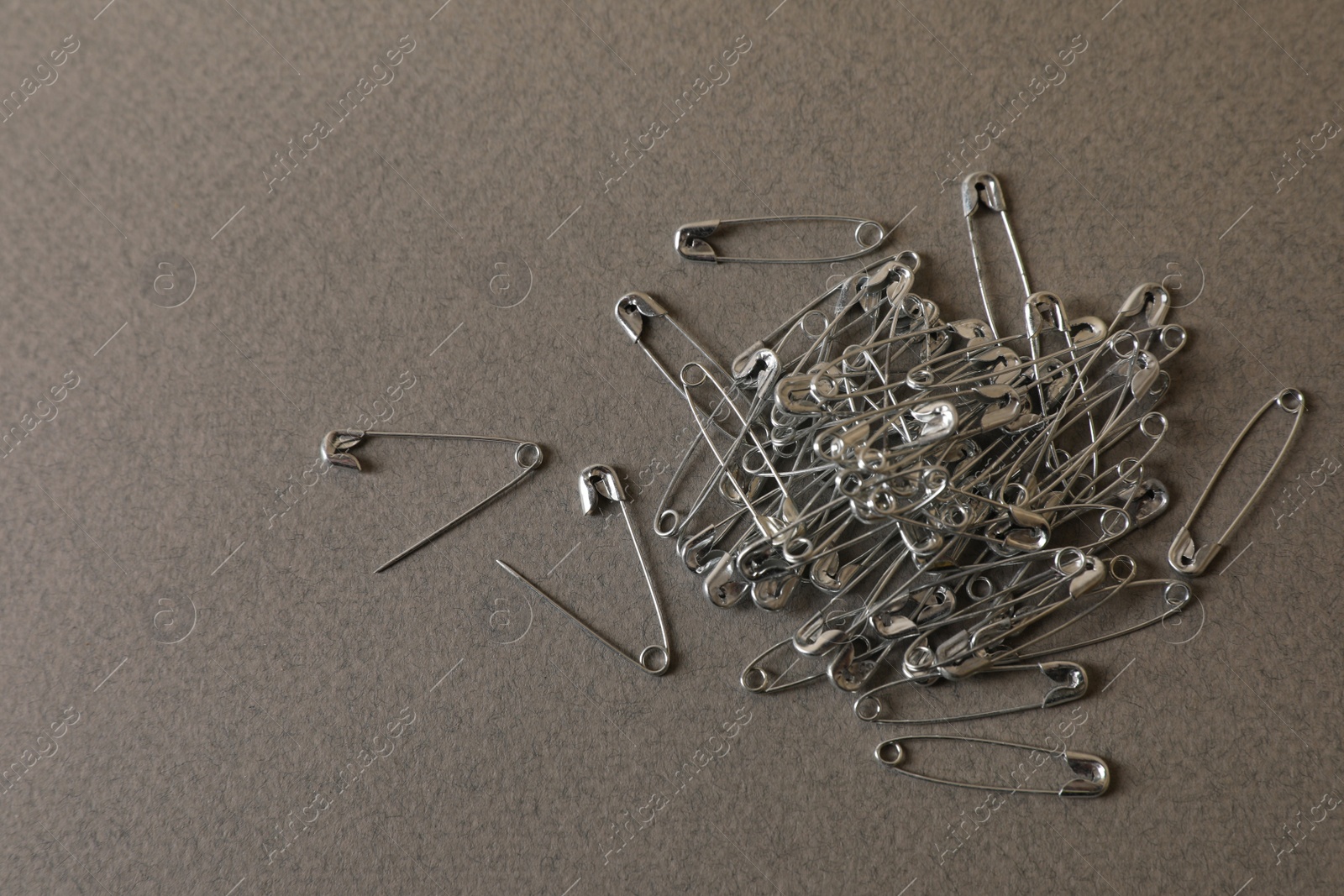 Photo of Pile of safety pins on grey textured background, flat lay