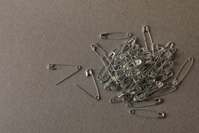 Pile of safety pins on grey textured background, flat lay