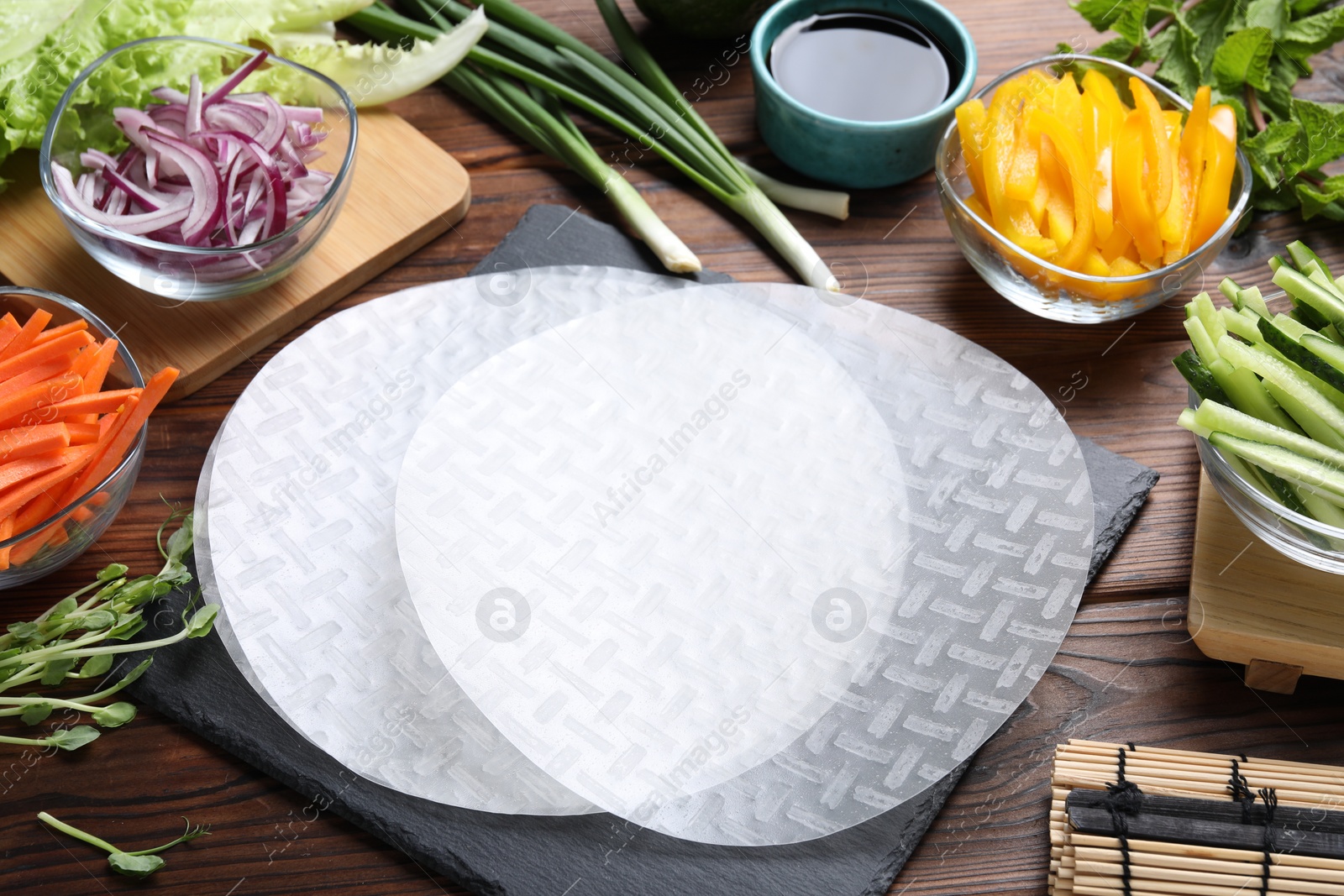 Photo of Rice paper, microgreens and other ingredients for spring rolls on wooden table, closeup