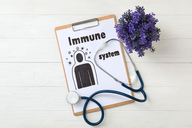 Photo of Clipboard with phrase Immune System, plant and stethoscope on white wooden table, flat lay