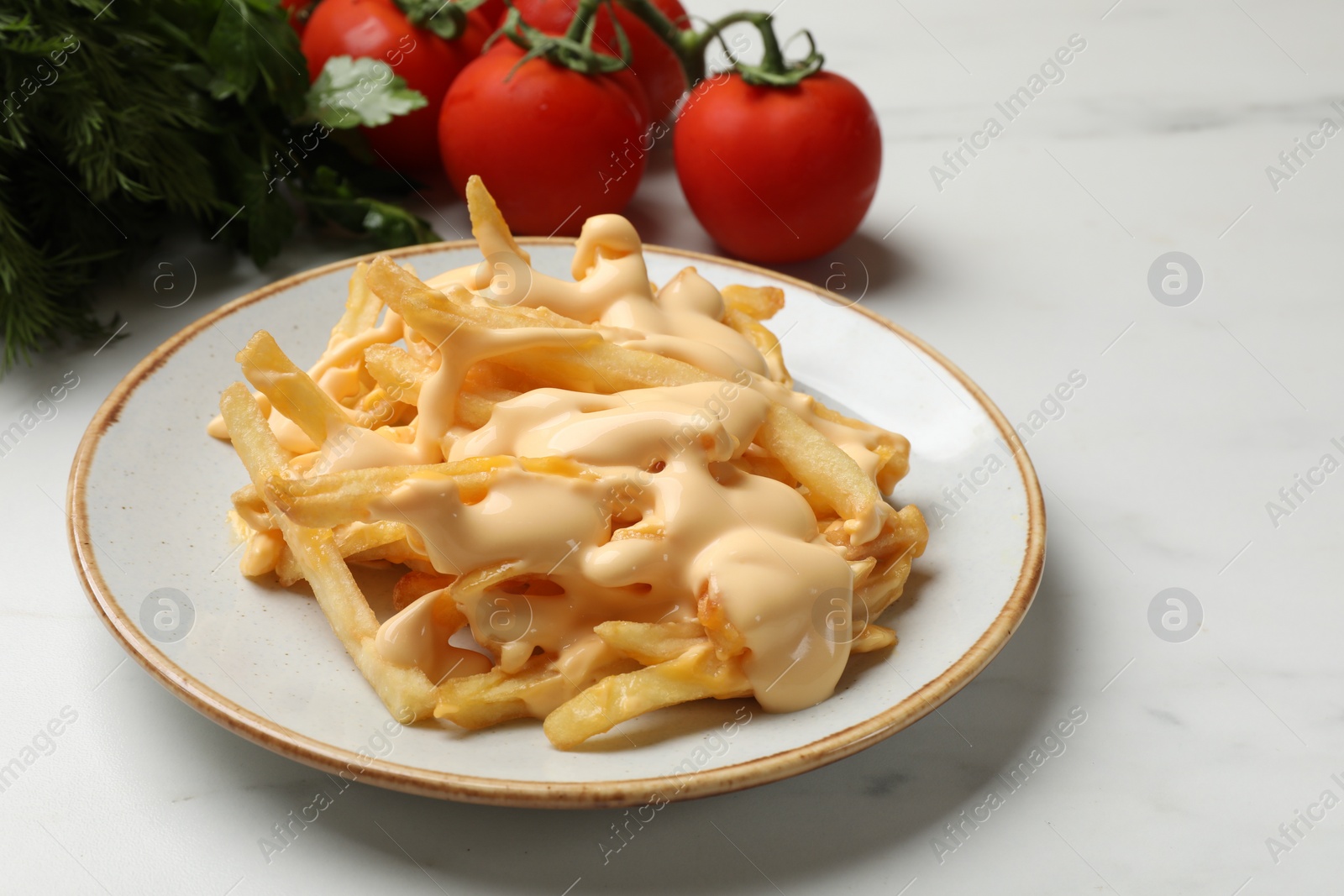 Photo of Delicious French fries with cheese sauce, tomatoes and dill on white marble table, closeup