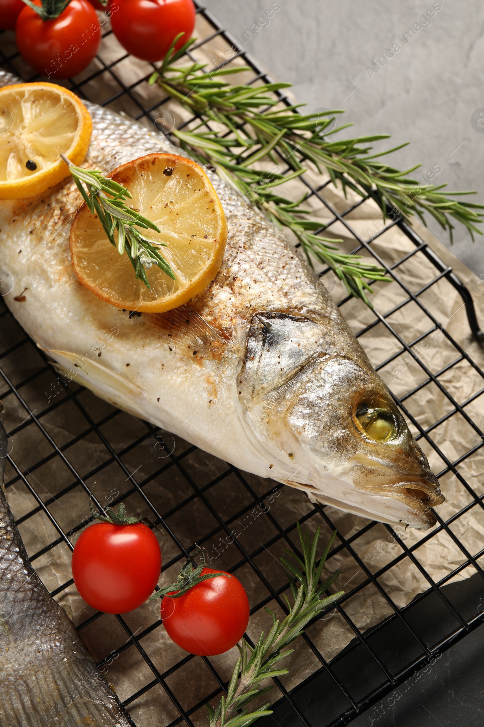 Photo of Baked fish with tomatoes, rosemary and lemon on black table, top view