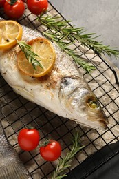 Photo of Baked fish with tomatoes, rosemary and lemon on black table, top view