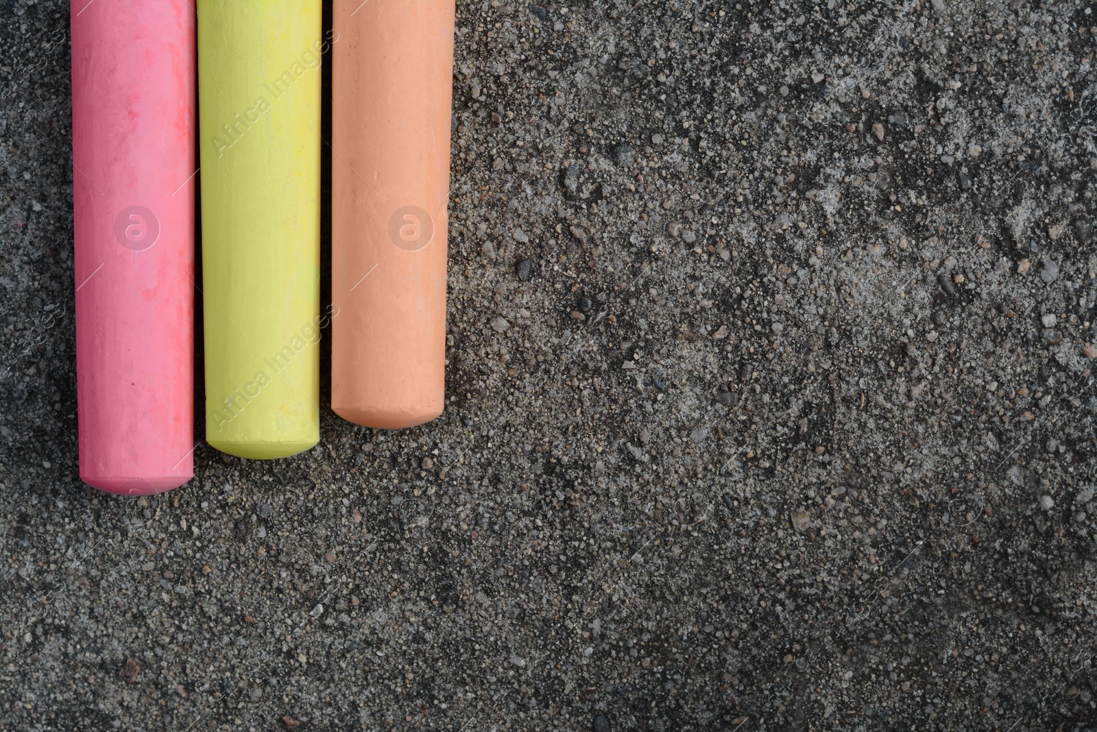 Photo of Colorful chalk sticks on asphalt, flat lay. Space for text