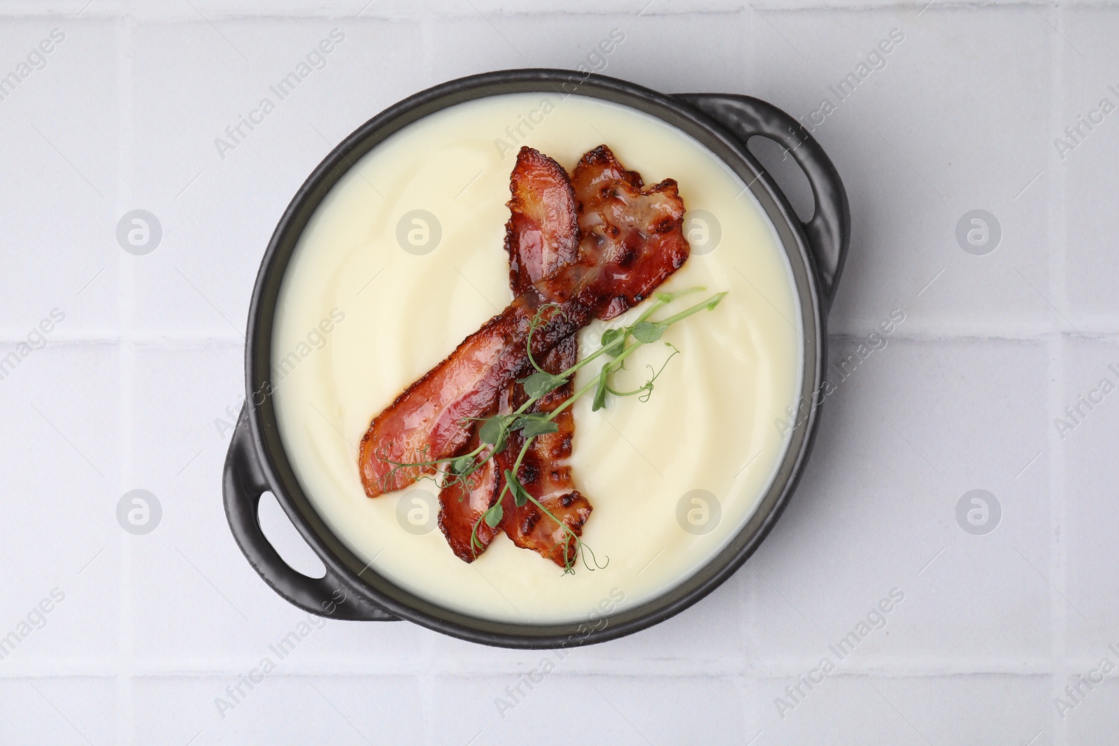 Photo of Delicious potato soup with bacon and microgreens in bowl on white tiled table, top view