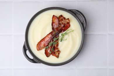 Delicious potato soup with bacon and microgreens in bowl on white tiled table, top view