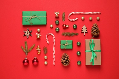 Photo of Christmas tree branches and festive decoration on red background, flat lay