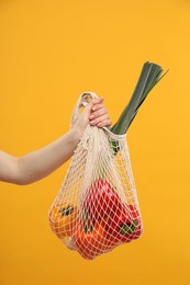 Photo of Woman with string bag of fresh vegetables on orange background, closeup