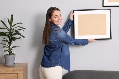 Woman hanging picture frame on gray wall at home