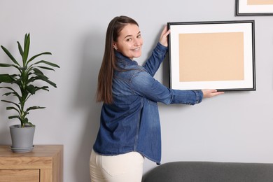 Photo of Woman hanging picture frame on gray wall at home