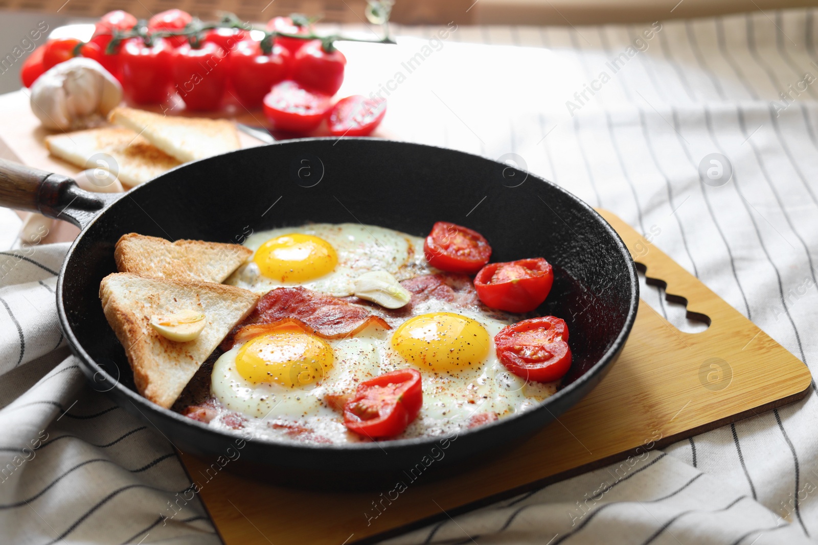 Photo of Delicious fried eggs with bacon and tomatoes in pan on table