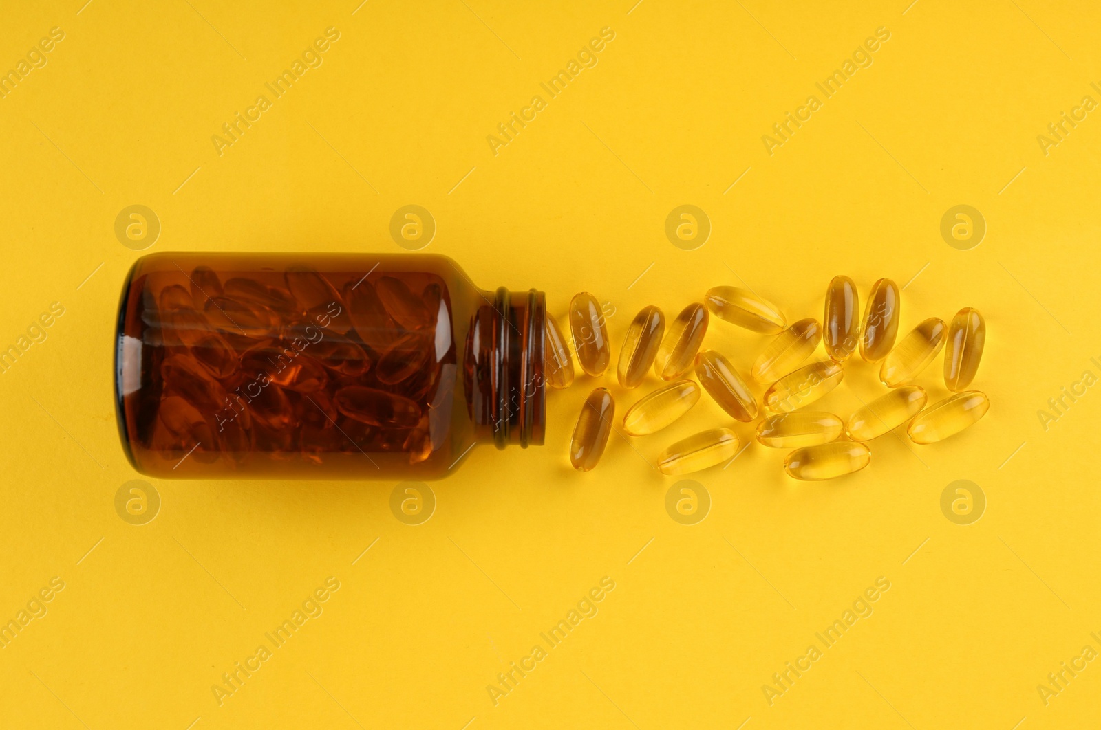 Photo of Glass medical bottle and vitamin capsules on yellow background, top view