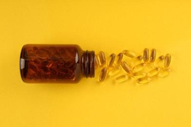 Photo of Glass medical bottle and vitamin capsules on yellow background, top view