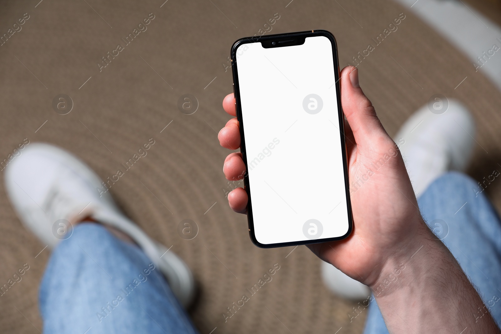 Photo of Man holding smartphone with blank screen indoors, closeup. Mockup for design