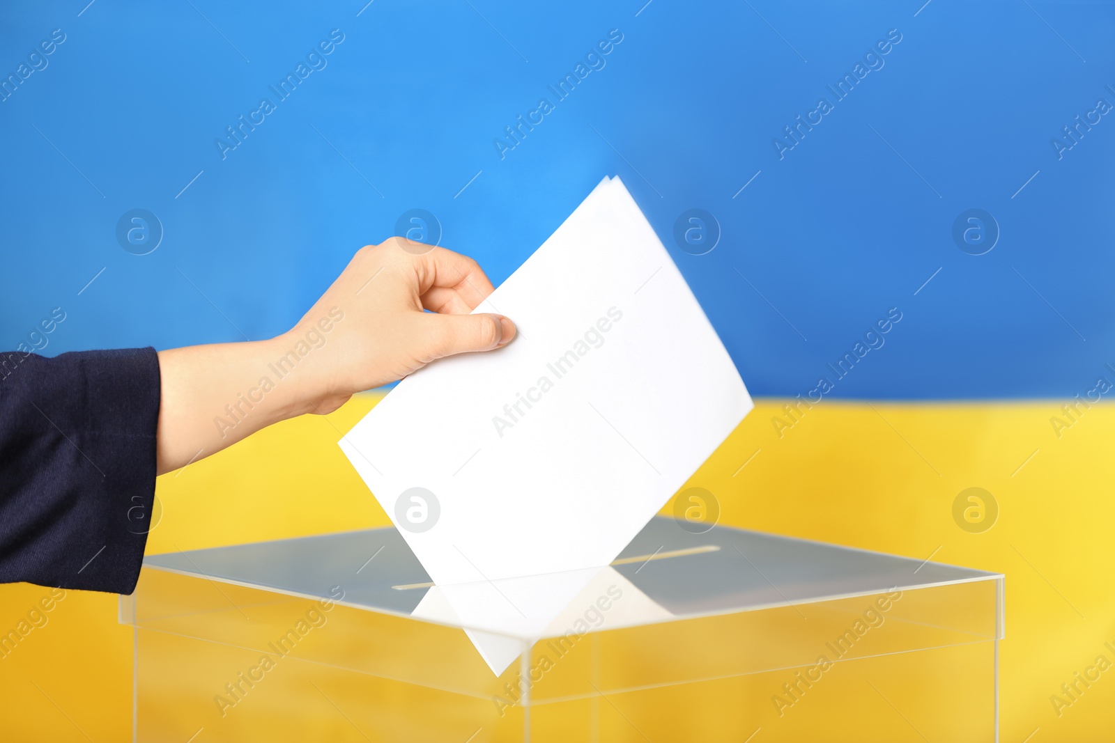 Photo of Woman putting voting paper into ballot box against Ukrainian flag, closeup