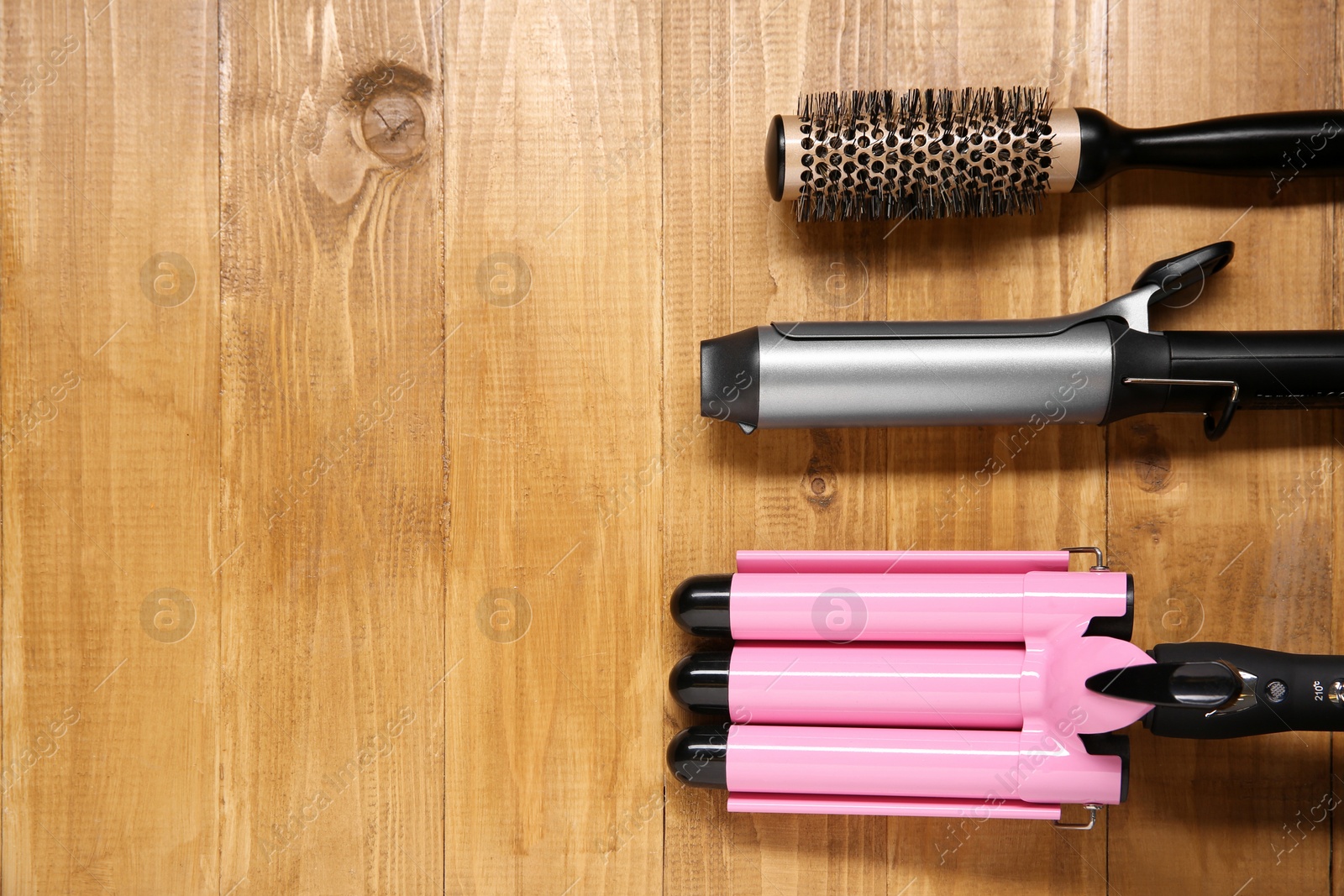 Photo of Different hair curling irons and round brush on wooden background, flat lay. Space for text