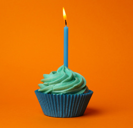 Delicious birthday cupcake with turquoise cream and burning candle on orange background