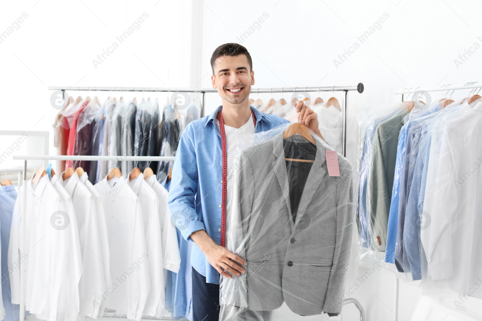 Photo of Young man holding hanger with jacket in plastic bag at dry-cleaner's