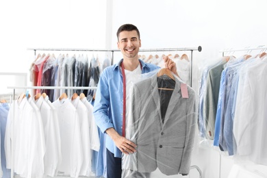 Photo of Young man holding hanger with jacket in plastic bag at dry-cleaner's