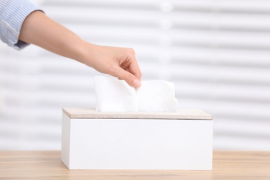 Photo of Woman taking paper tissue from holder on light background, closeup