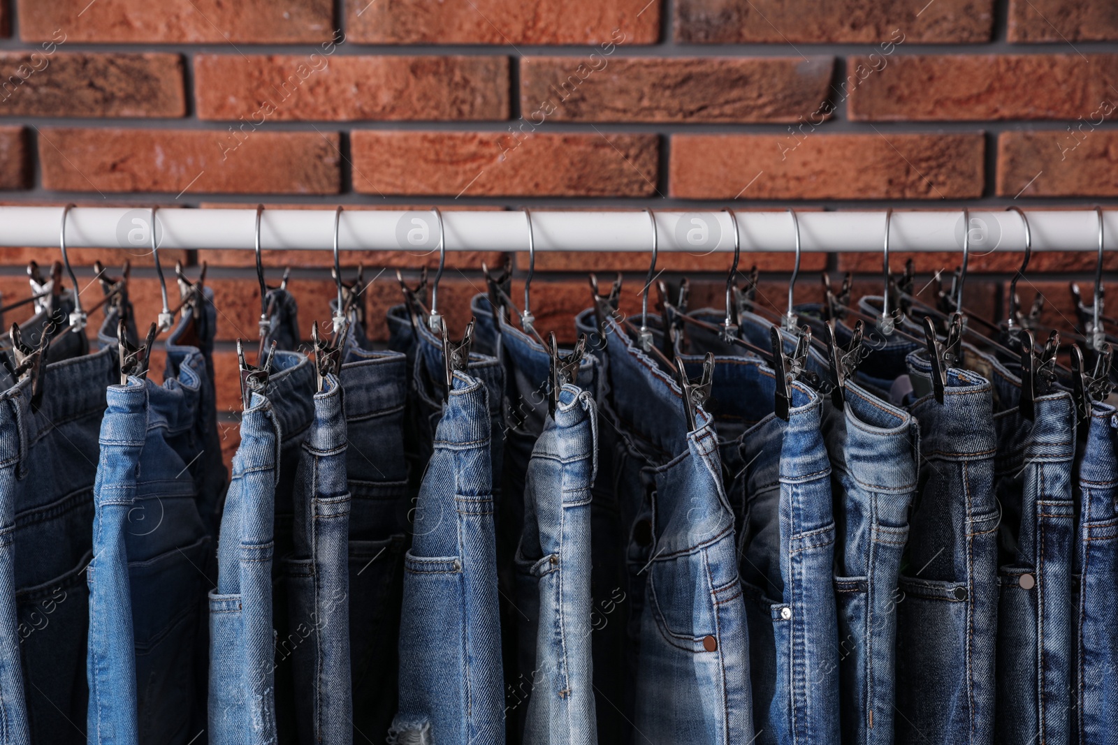 Photo of Rack with stylish jeans near brick wall, closeup